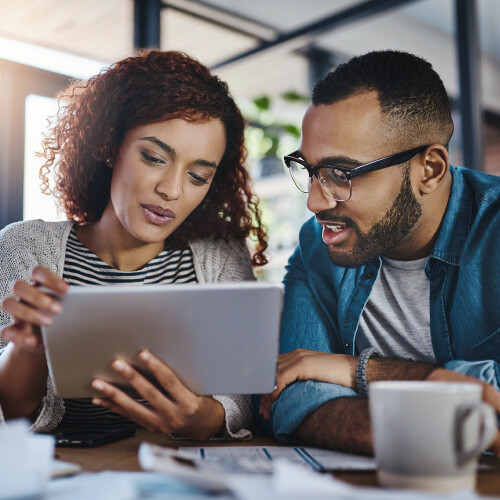 Two people looking at a tablet, sitting at a table with a coffee mug and papers.