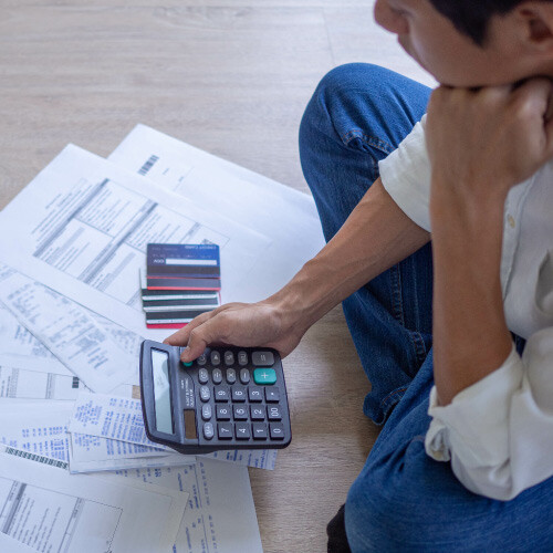  Person sitting on the floor with papers and credit cards, using a calculator.