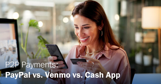 Woman smiling, holding a smartphone and credit card at a desk.