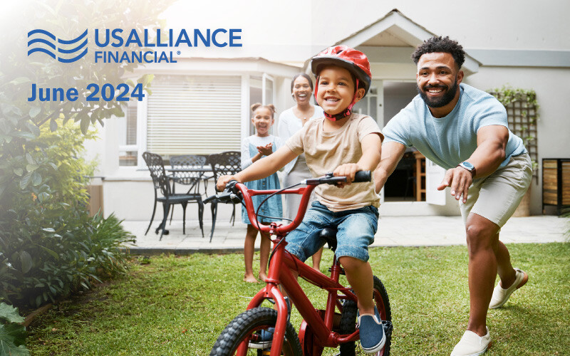 Family in a backyard with a boy on a red bike and a man running beside him, with a woman and girl in the background.