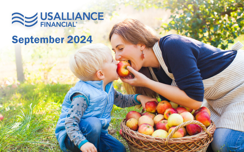 Woman and young boy sharing an apple in an orchard, basket of apples beside them. Text in Image: USALLIANCE FINANCIAL® September 2024.