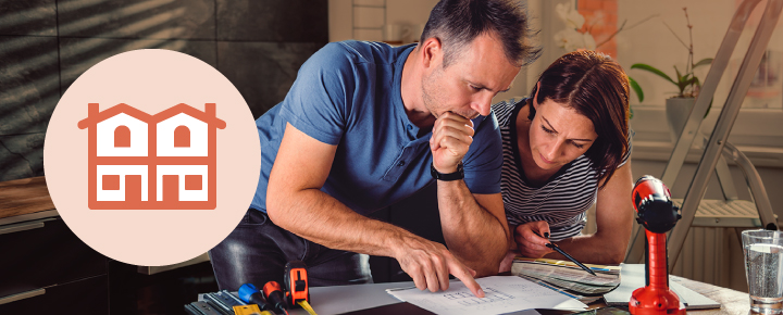 A couple lean over some work plans surrounded by construction tools.