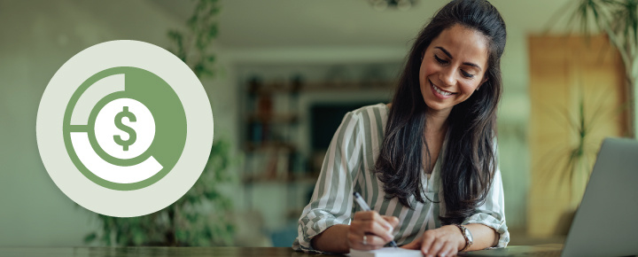 Woman smiling and writing at a table with a laptop.