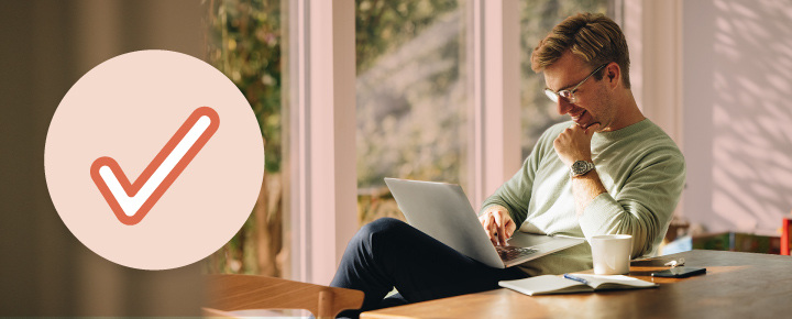 Man working on a laptop at a table with a cup, notebook, and pen, next to a circular icon with a red tick mark.