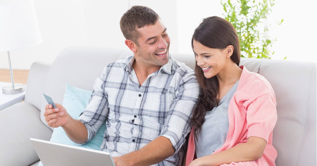 Husband and wife excited in their living room using their Classic Visa credit card to online shop.