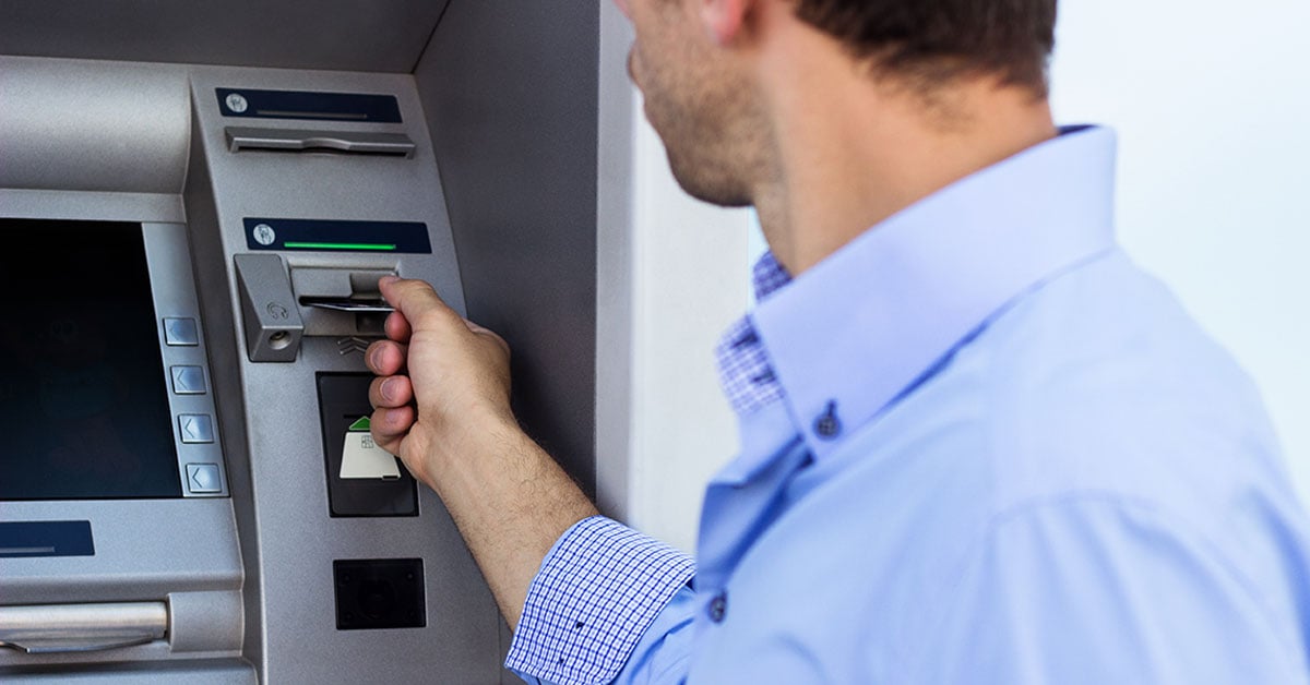 Business dressed man placing his atm card into the atm machine.