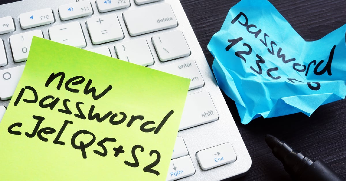 A yellow and blue sticky note with passwords written down in black marker ontop of computer keyboard.