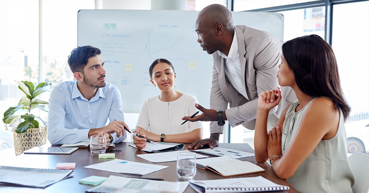A group of employees have a discussion around a board room table.