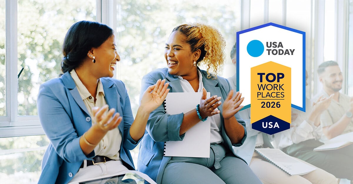 Two employees smile at each other while clapping, a USA Today workplace award in the background.