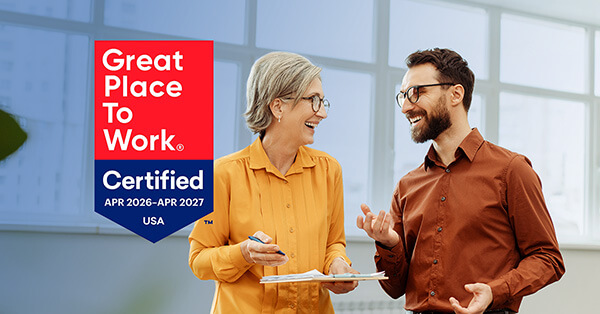 Two coworkers laugh and talk, with the Great Place to Work Certified 2026 Banner on top.