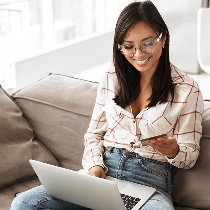A woman looking at her credit card, and paying down her debt on her laptop.