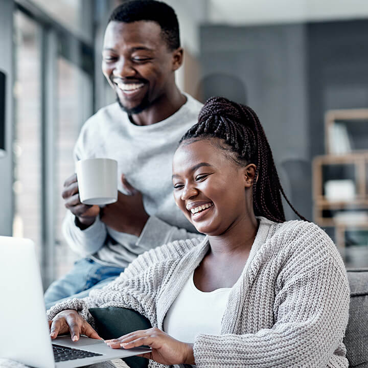 A man and a woman reviewing their savings on a laptop and drinking coffee.