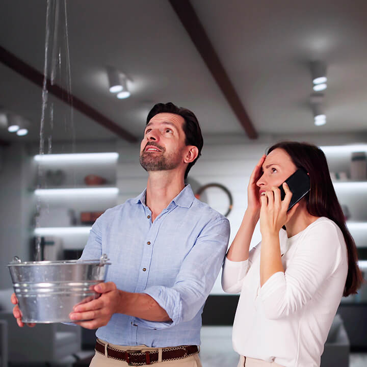 A man and woman holding a bucket to catch water leaking from the ceiling.