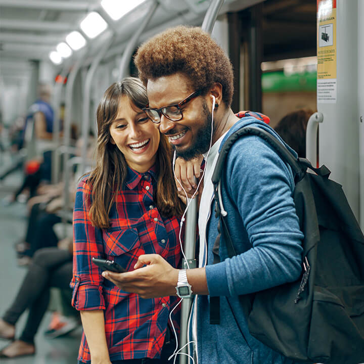 A man and woman transfer funds on a smartphone insdie a subway train.